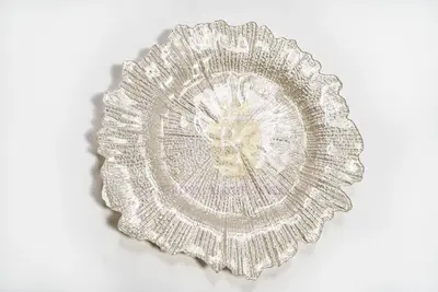Pearl white glass charger with an irregular ruffled edge and ribbed radial texture, top-down view