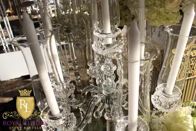 Close-up of white taper candles in clear glass tulip shades on a crystal candelabra, with white hydrangeas behind
