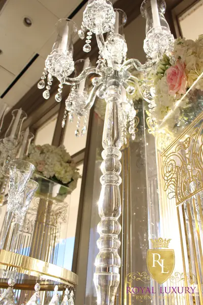 Tall crystal candelabra with beaded stem and hanging drops, seen from below among gold-etched pillars and flowers