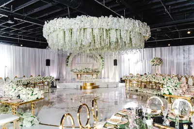 Curved gold tables dressed with white flowers and gold chairs around a dance floor under a hanging flower canopy at a wedding