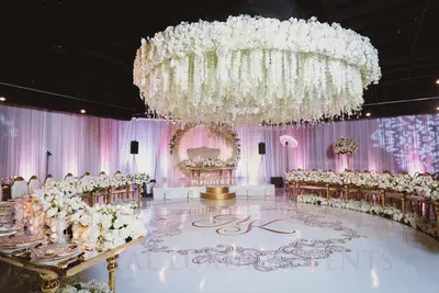 Curved gold tables with white floral centrepieces framing a monogrammed dance floor, styled at an evening wedding reception