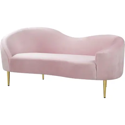 Blush pink suede curved loveseat with slim gold legs, shown at a three-quarter angle
