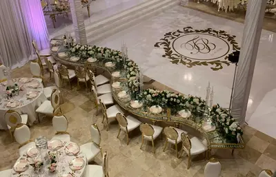 S-shaped gold and glass table seen from a balcony, set with place settings and flowers beside a monogrammed dance floor