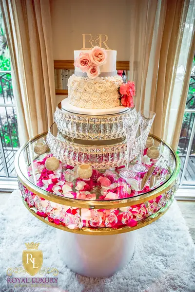 Overhead view of gold-rimmed round glass table with pink petals under the glass, styled with a tiered rose wedding cake