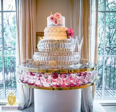 Gold-edged crystal cake table with white base and rose petals beneath the glass, styled with a tiered wedding cake