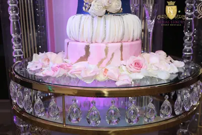 Close-up of gold-rimmed glass table top with hanging crystal teardrops, set with a pink marbled cake and roses