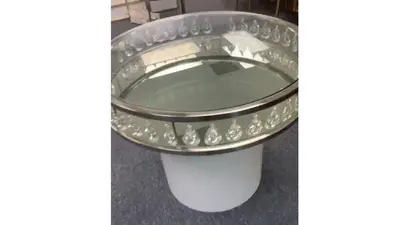 Round table with silver-toned rim and mirrored top, crystal drops around the edge and white base, shown in a showroom