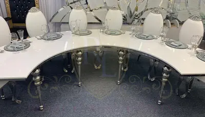 Curved white-topped table with silver bubble legs, set with place settings and white chairs at an event