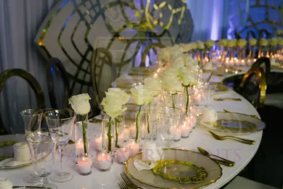 Close-up of a white table set with white roses, tealight candles, wine glasses and gold-rimmed plates