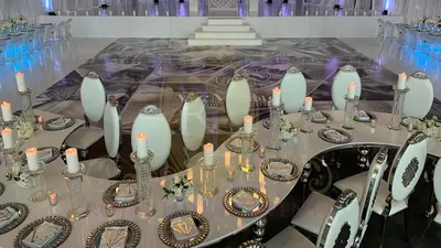 Curved white serpentine table with tall candles and mirrored charger plates facing a patterned dance floor and white steps