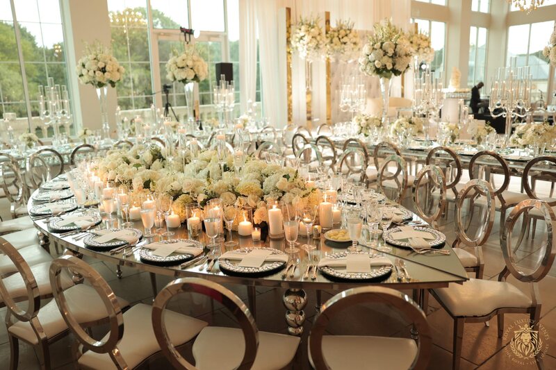 Round mirrored table with gold-rimmed chargers, white floral centerpiece and candles, surrounded by gold oval-back chairs