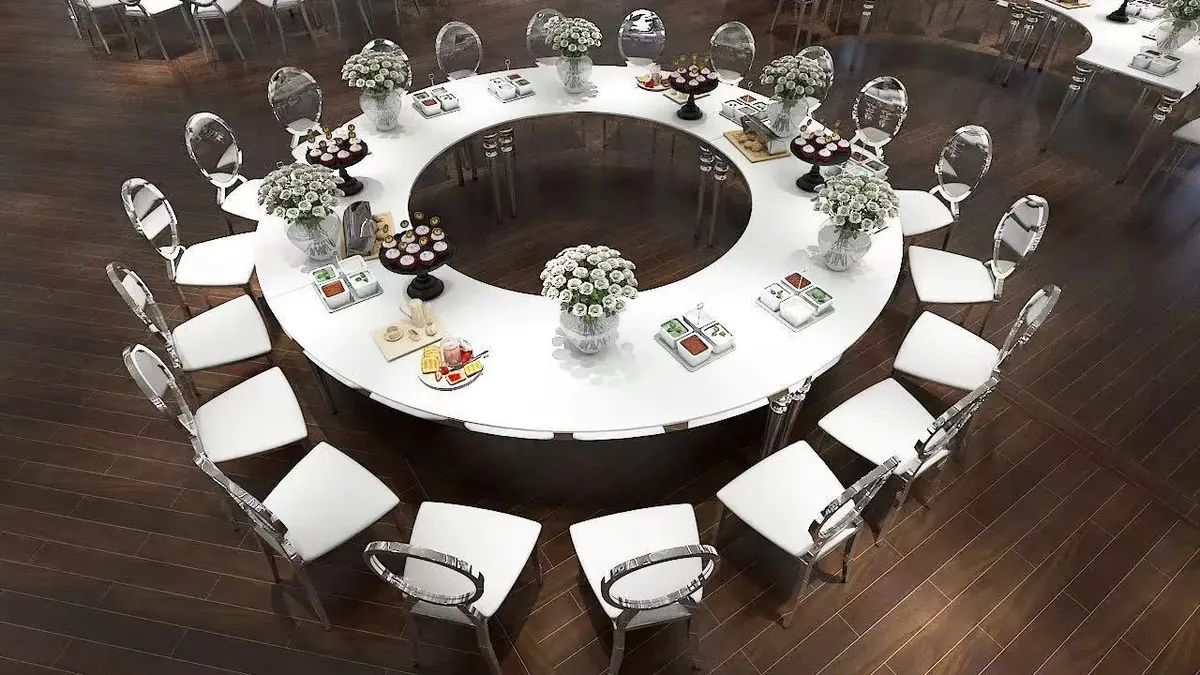 Aerial view of a white glossy circular table with silver frame and clear chairs, set with flowers and desserts