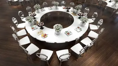 Overhead view of a white circular table with an open centre, set with chairs, flower vases and dessert platters