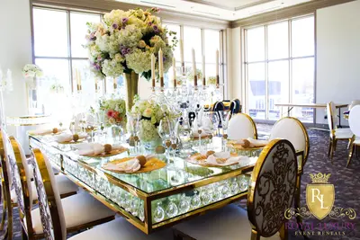 Gold-framed glass-top table with crystal drops, set with white hydrangeas, candelabra and napkins at a reception