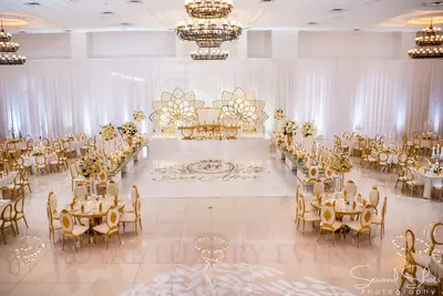 Two long gold and crystal tables lining a white dance floor in a ballroom, with a gold sweetheart stage at the far end