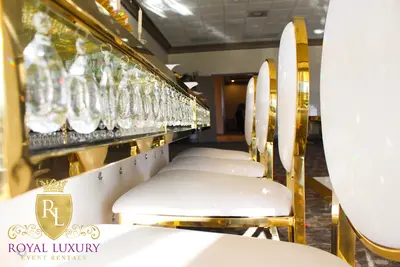 Low angle along the table's crystal-hung glass edge, with white and gold round-back chairs lined up beside it