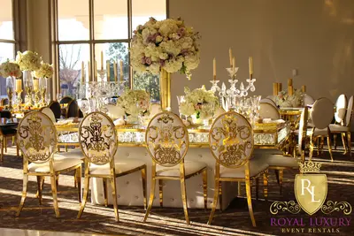 Gold-framed table with white tufted base, floral centerpieces and candelabra, seen behind white and gold damask-back chairs