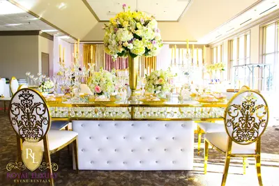 White tufted table base with crystal buttons, gold-framed glass top, tall hydrangea centerpiece and candles, styled at a
