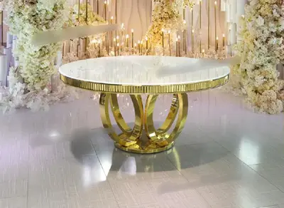 Round white-topped table with gold dentil edging and interlocking gold ring base, shown against white floral arrangements