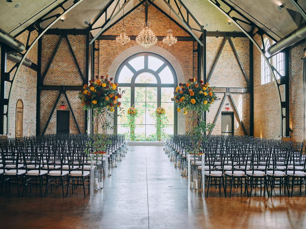 luxurious indoor wedding ceremony decor design, with a large red, yellow, and orange floral designs and a colorful bridal bouquet.