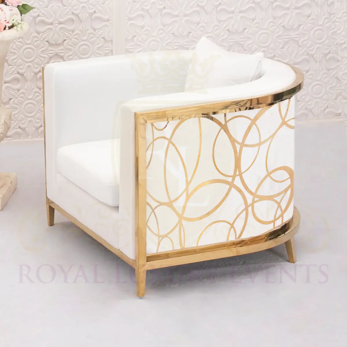 White lounge chair with curved back, gold frame and interlocking gold circle design on the side, against a patterned white