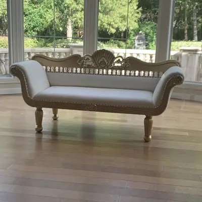 Matte gold loveseat with white leather seat, carved shell crest and spindle back, on hardwood floor
