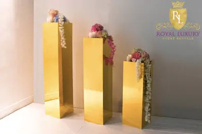 Three gold mirrored flower stands topped with pink and white blooms, candles and trailing wisteria, styled beside a corner