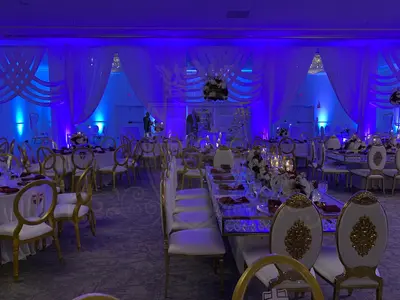 Ivory draped ballroom wall with woven swag details, washed in blue uplighting over gold chairs and reception tables