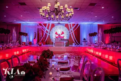 Red and white draped stage backdrop with a round white centrepiece, lit in magenta and blue over a long reception table
