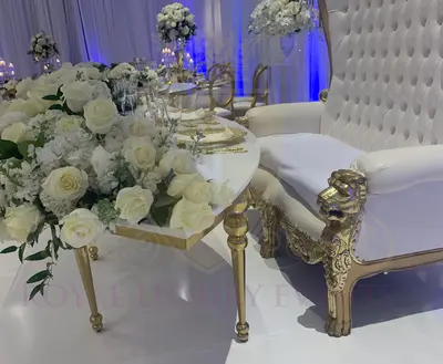 Close-up of a gold bubble-legged table with white top and white rose arrangement beside a tufted white and gold lion-arm sofa