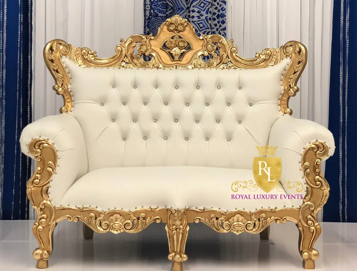 Gold throne loveseat with ivory tufted leather back and carved frame, set against white and blue drapes