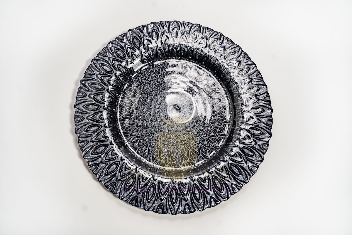 Overhead view of a black glass charger with a scalloped rim and feather-pattern etching