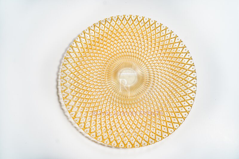 Round gold glass charger seen from above, with a radiating diamond lattice pattern and a ribbed clear centre