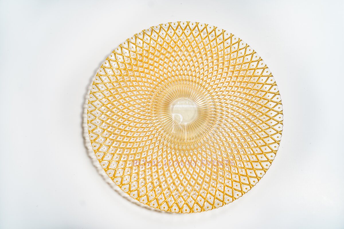Round gold glass charger seen from above, with a radiating diamond lattice pattern and a ribbed clear centre