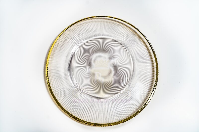 Clear ribbed glass charger plate with a gold rim, photographed from above