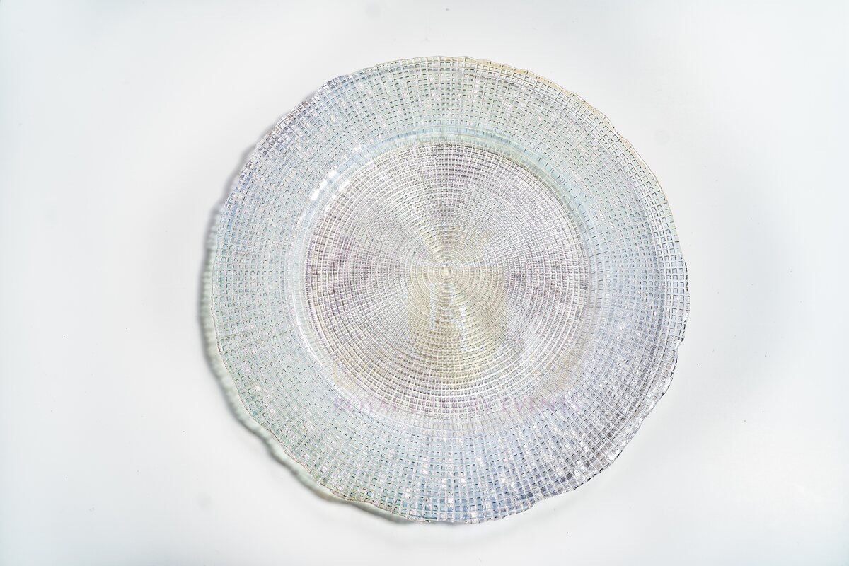 Clear iridescent glass charger plate seen from above, with a fine woven grid texture and softly scalloped rim