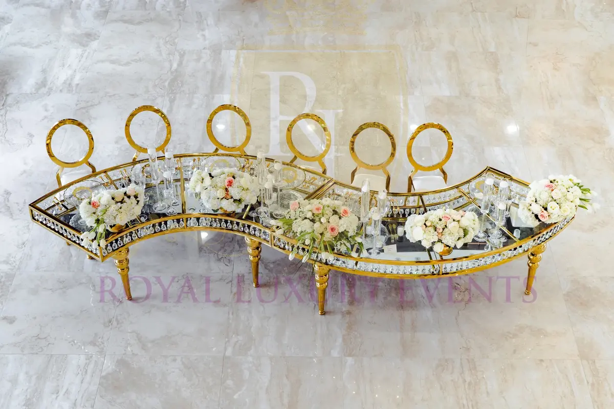 Gold serpentine table with crystal-edge glass top, seen from above with white and blush floral arrangements and gold