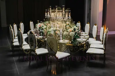 Gold teardrop table with mirror top and candle centrepiece, styled at an evening reception with white gold-trimmed chairs
