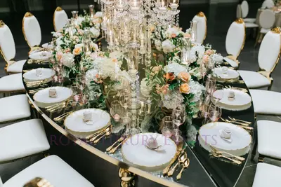 Close-up of a teardrop table's mirrored top reflecting white plates, gold cutlery, blush glasses and peach roses