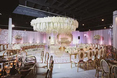 Teardrop tables with gold frames in a wedding ballroom beneath a large hanging white floral installation and draped walls