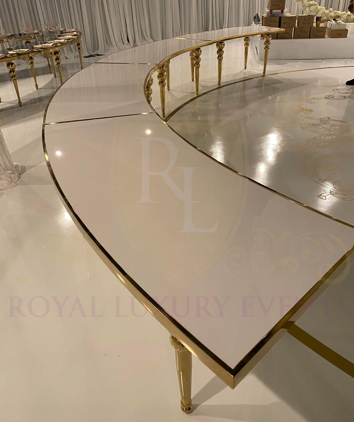 Curved white glossy table with gold polished steel edge and turned gold legs, shown in a bare setup on a white floor