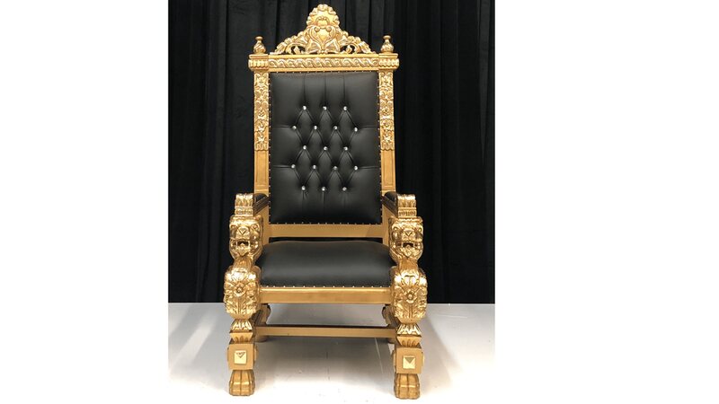 Gold throne chair with black tufted leather backrest and seat, carved lion armrests, front view against a black curtain