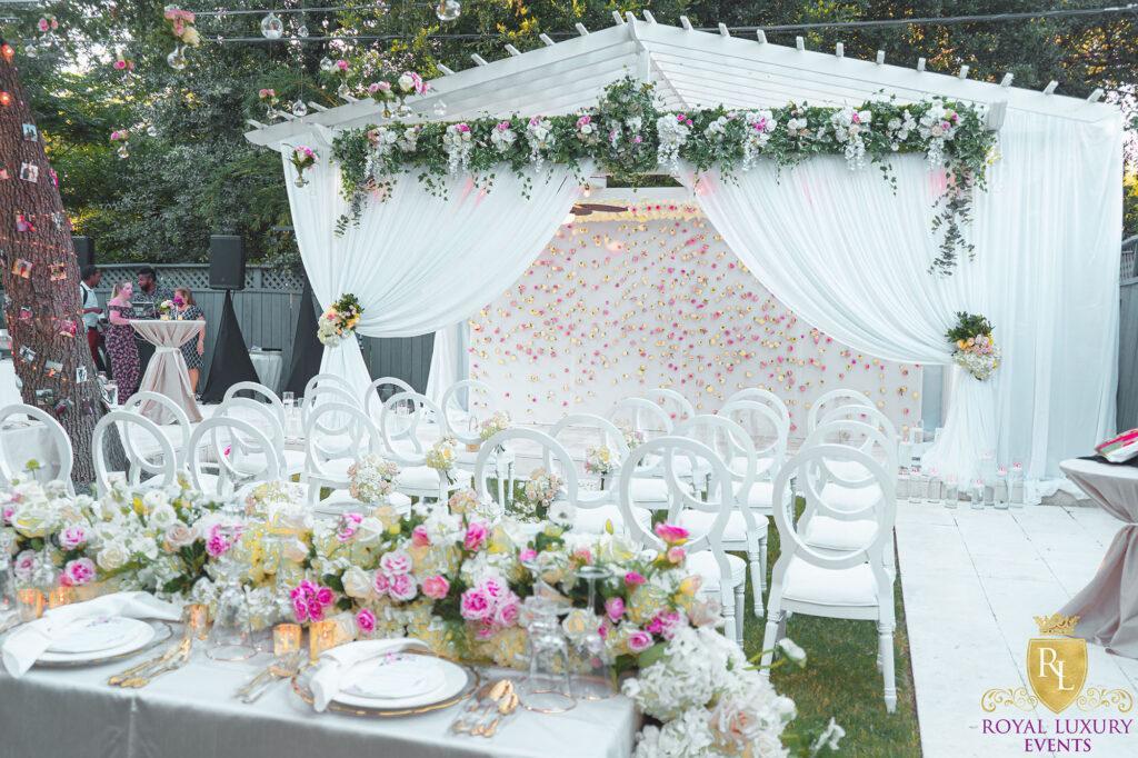 intimate backyard wedding decor featured pastel florals, white chairs, a greenery wall, and many other unique details