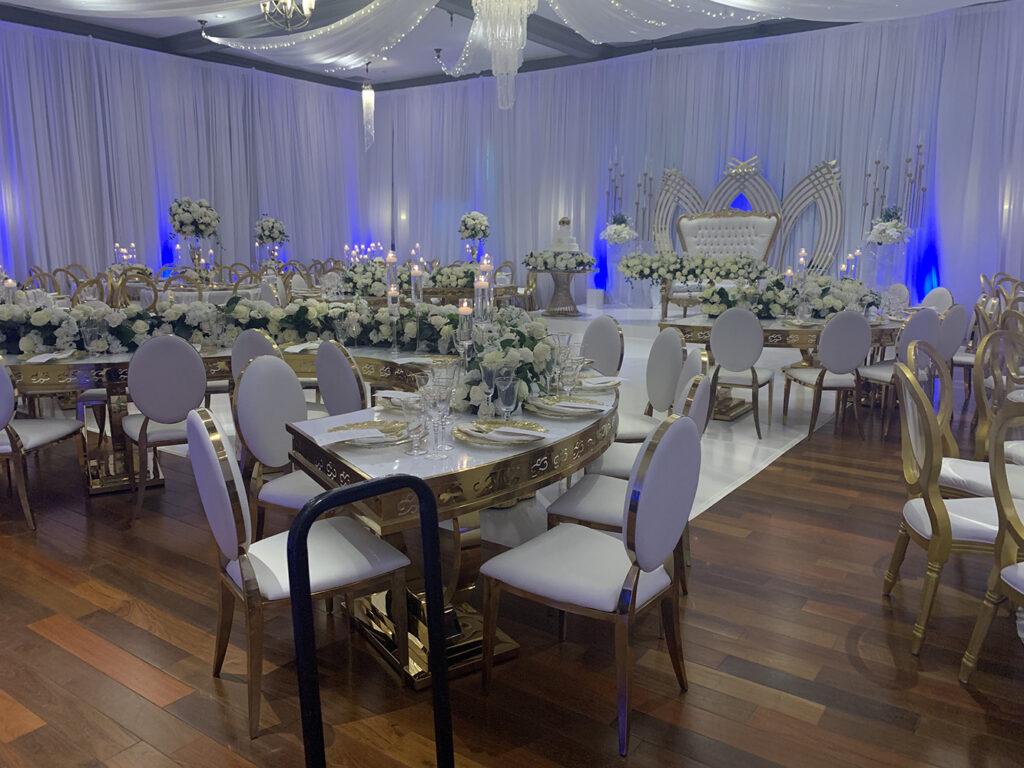 View this September 2019 Wedding in Dickinson, TX at NOAH’s Event Venue. Featuring gold and white wedding decor, with blue uplighting.