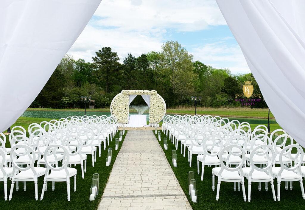 all white wedding ceremony decor featuring floral arch and candles on the aisle
