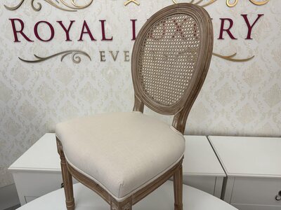 Wooden Louis chair with woven mesh back and cream seat, angled view in the showroom against a damask wall
