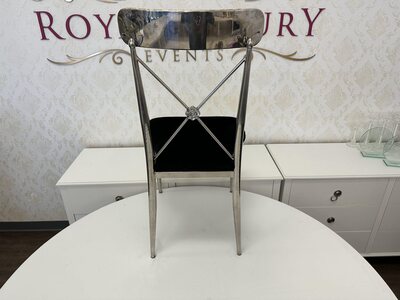 Rear view of silver cross-back chair showing the X-shaped metal back with a small rosette and black velvet seat