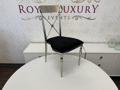 Silver cross-back chair with black velvet seat on a white round table in the showroom, front three-quarter view