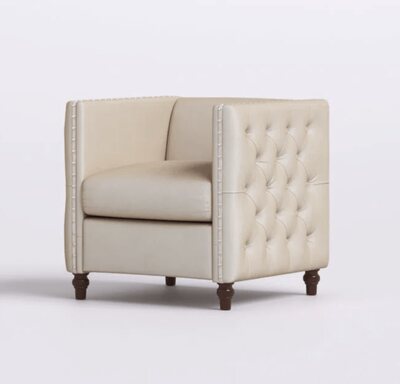 Single beige tufted armchair with nailhead trim and dark turned wood legs, angled to show the side tufting