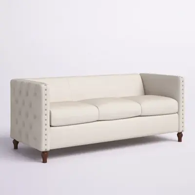 Beige three-cushion sofa with tufted side arm, nailhead trim and turned dark wood legs, shown on a plain backdrop